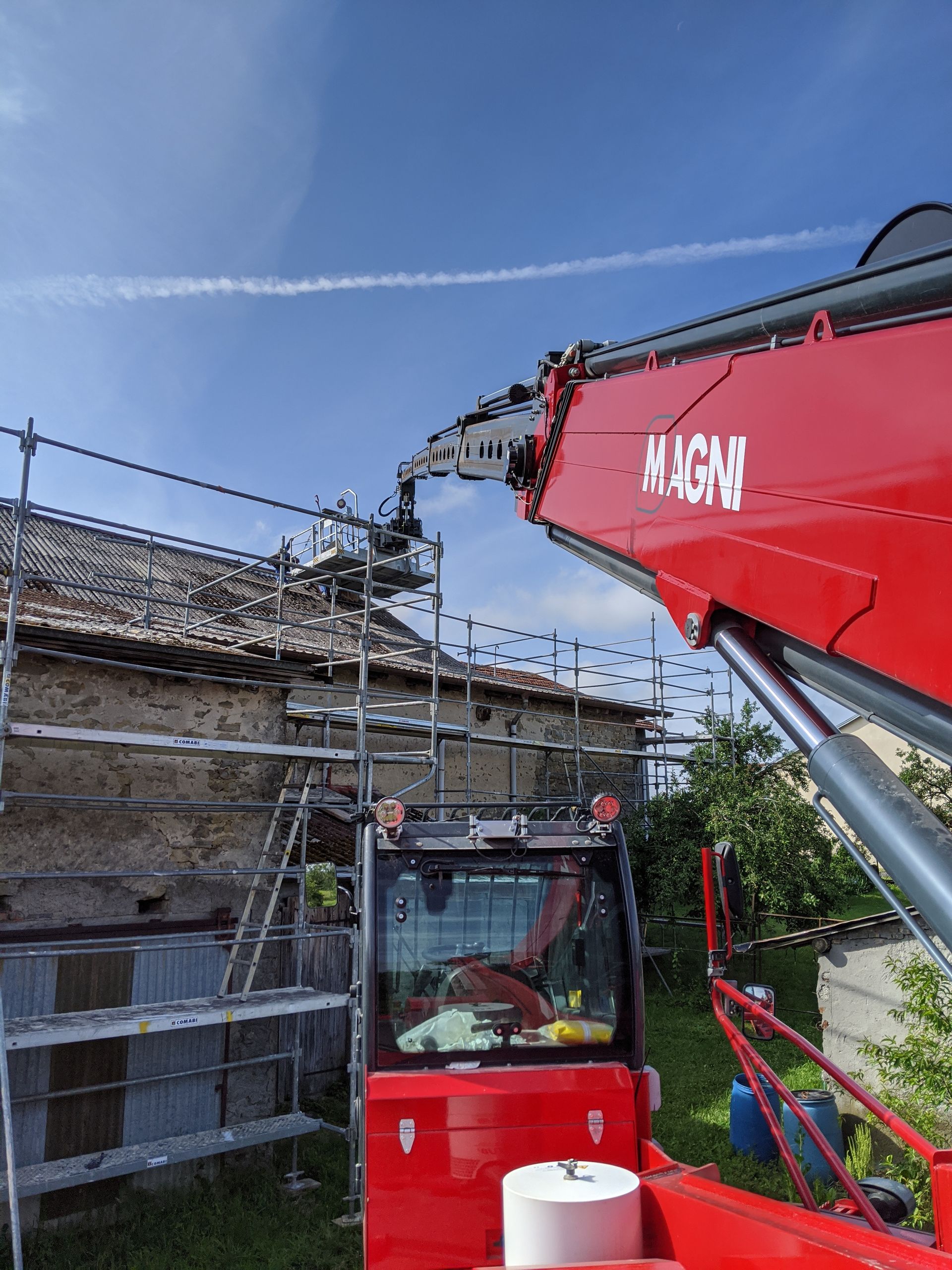 Zoom sur la nacelle d'un bras télescopique avec intervention sur le toit d'une vieille maison et échaffaudage autour de la maison