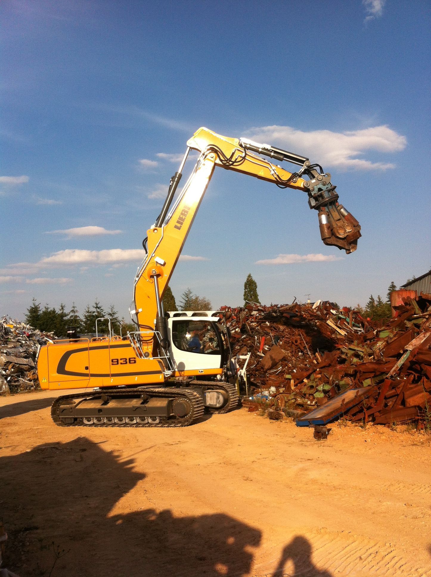 Tractopelle Liebherr jaune avec pince de destruction au milieu de déchets métalliques