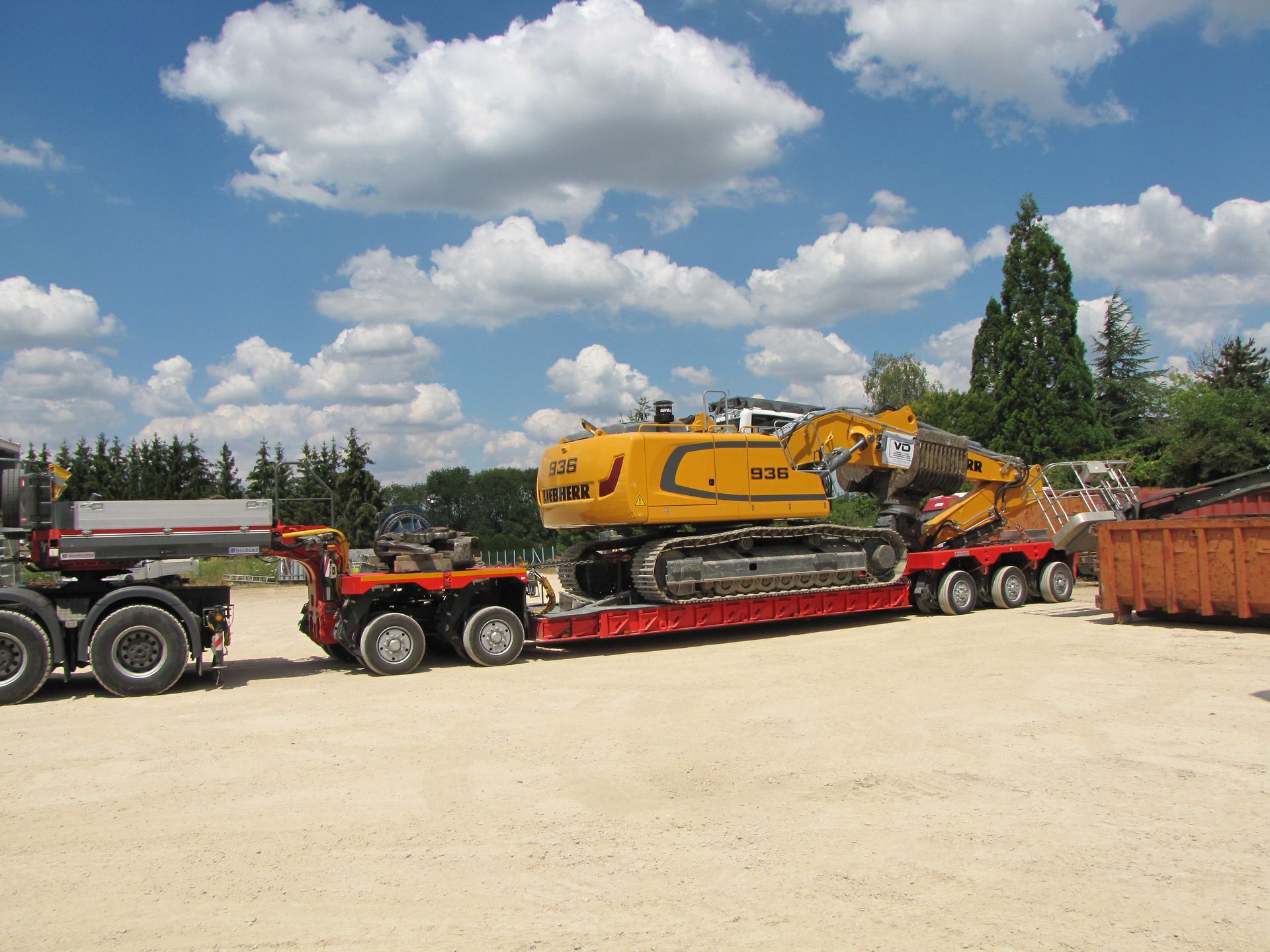 Tractopelle Liebherr jaune sur la remorque d'un camion rouge avant départ