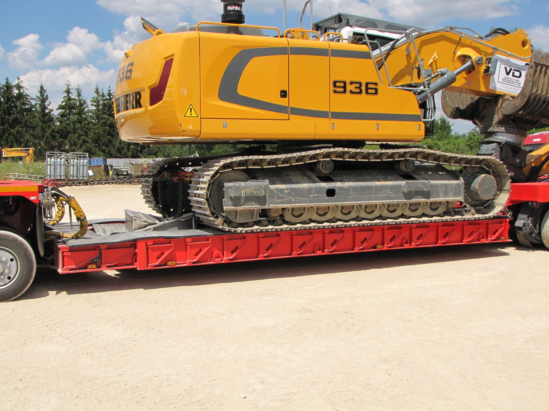Tractopelle Liebherr jaune sur la remorque d'un camion rouge