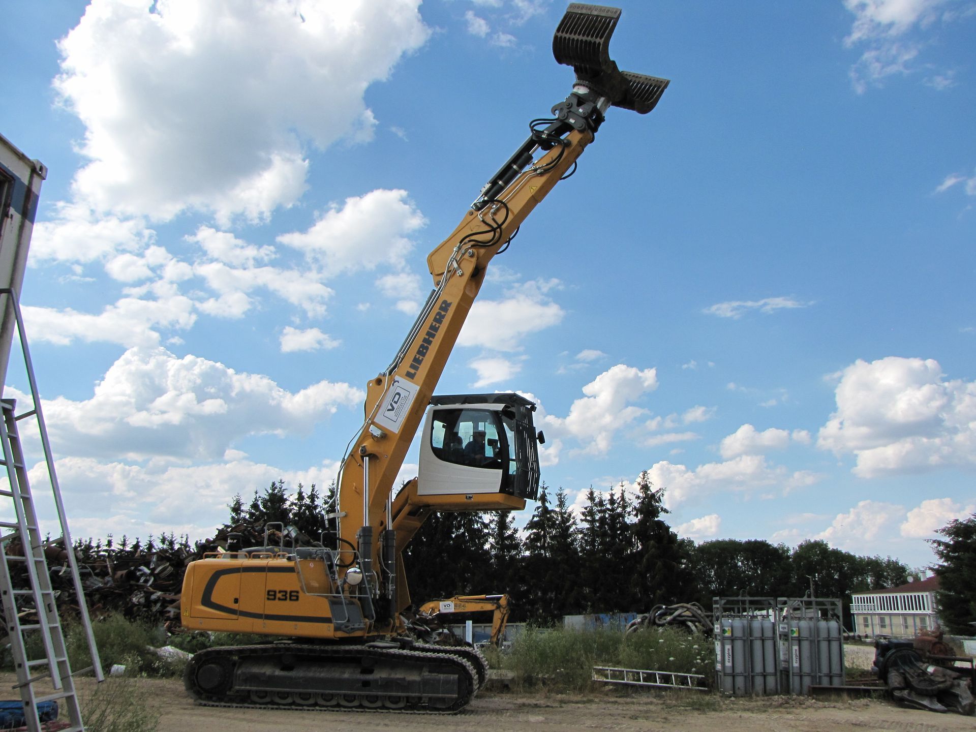 Tractopelle Liebherr jaune avec pince complétement déployé vers le haut pour atteindre une grande hauteur