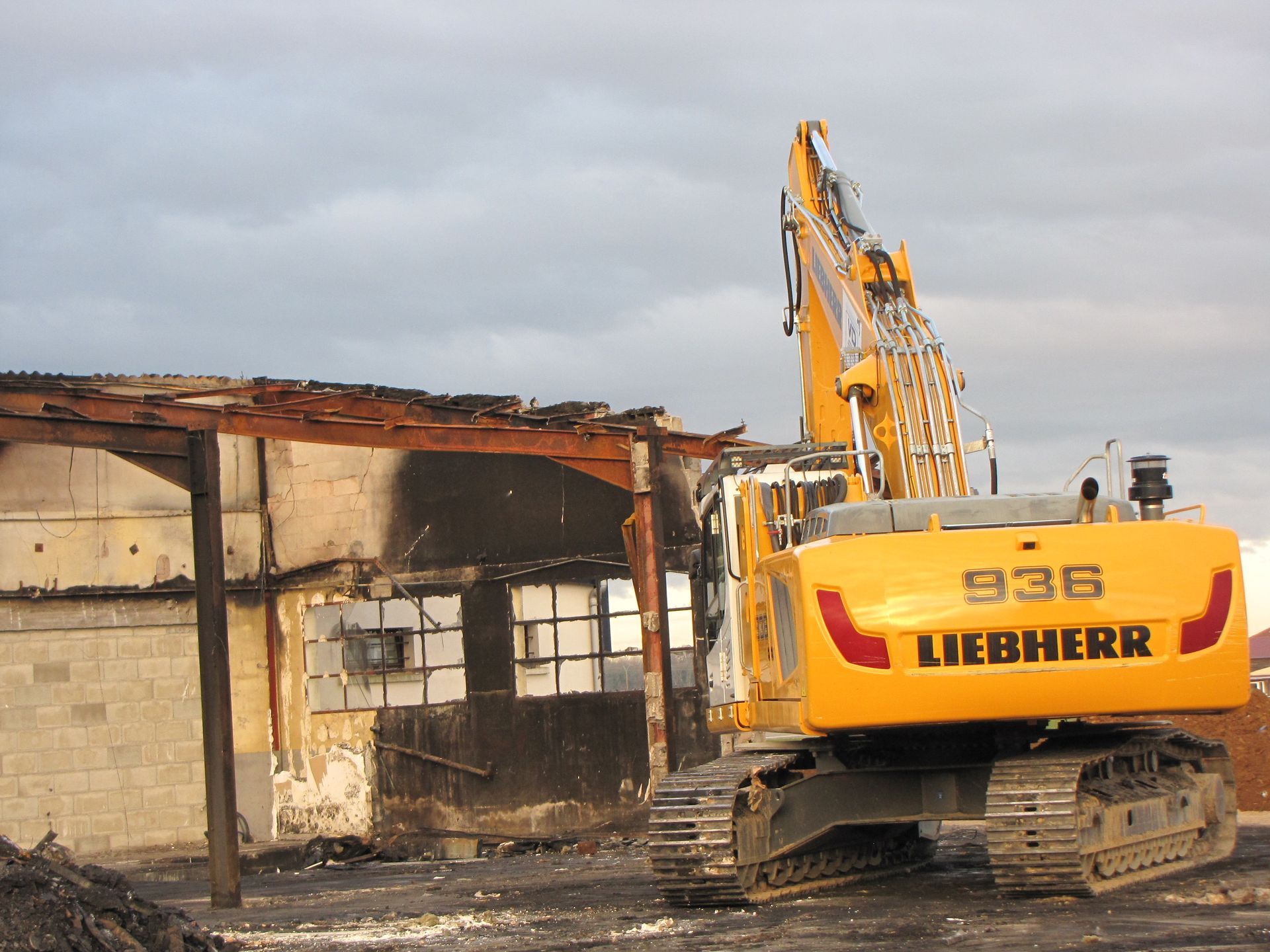Tractopelle Liebherr jaune avec pince vue de derrière en action sur un bâtiment 