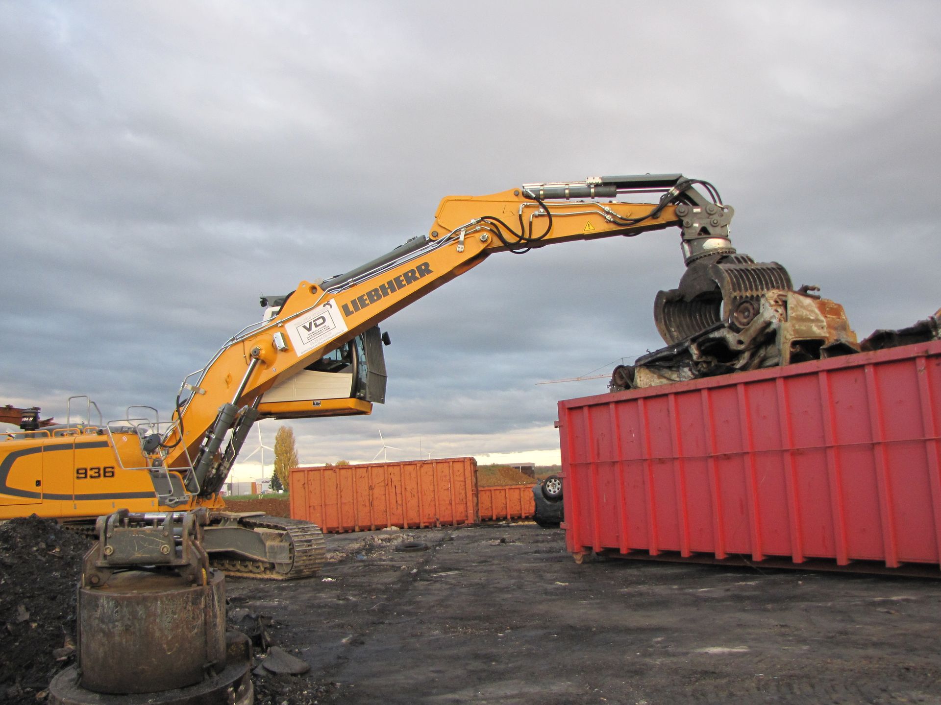 Tractopelle Liebherr jaune avec pince en train de déposer des déchets dans une benne rouge
