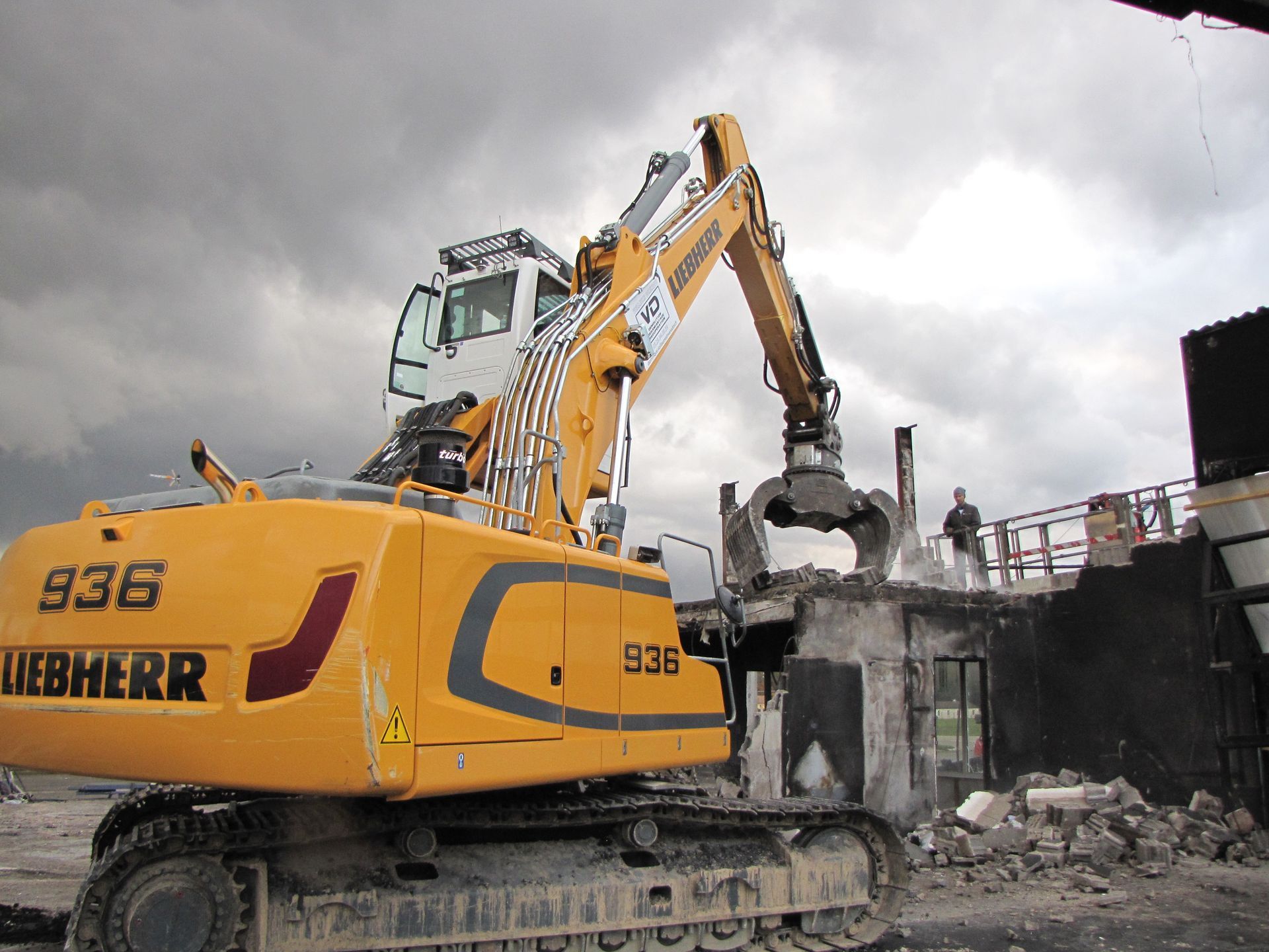 Tractopelle Liebherr jaune avec pince en train de détruire un batiment