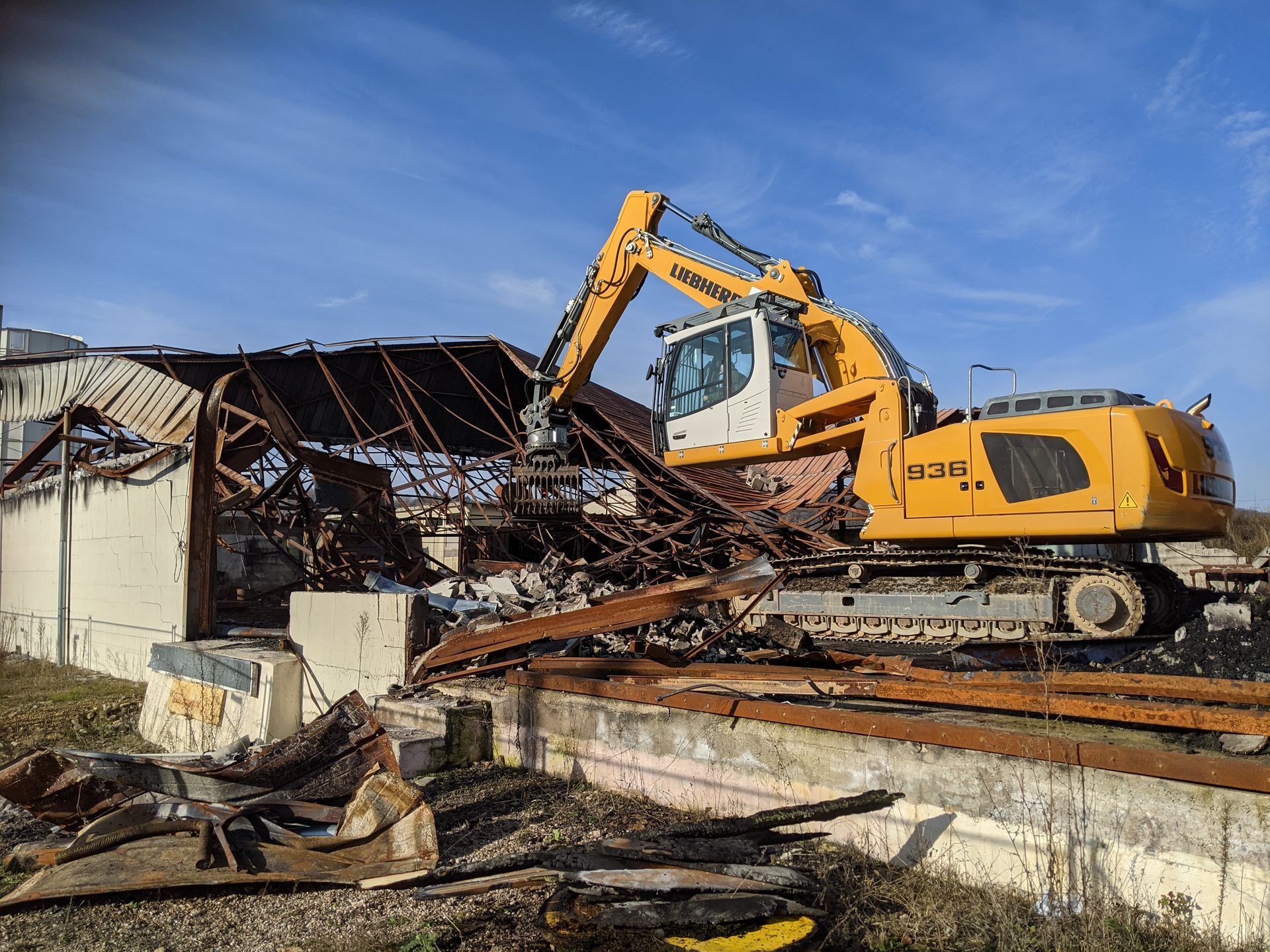 Tractopelle jaune en train de détruire une structure métallique d'un ancien bâtiment d'entreprise