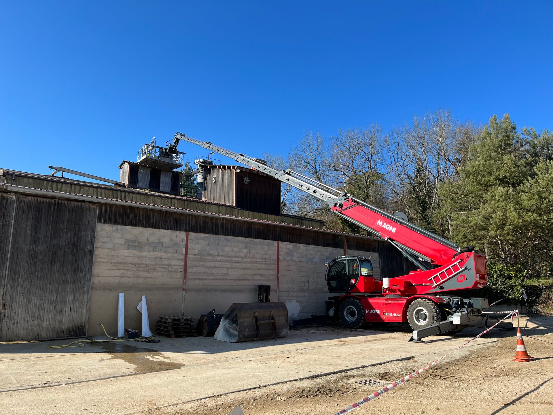Chariot rouge Magni monté sur stabilisateur araignée avec nacelle déployée sur le bâtiment d'une usine désaffecté