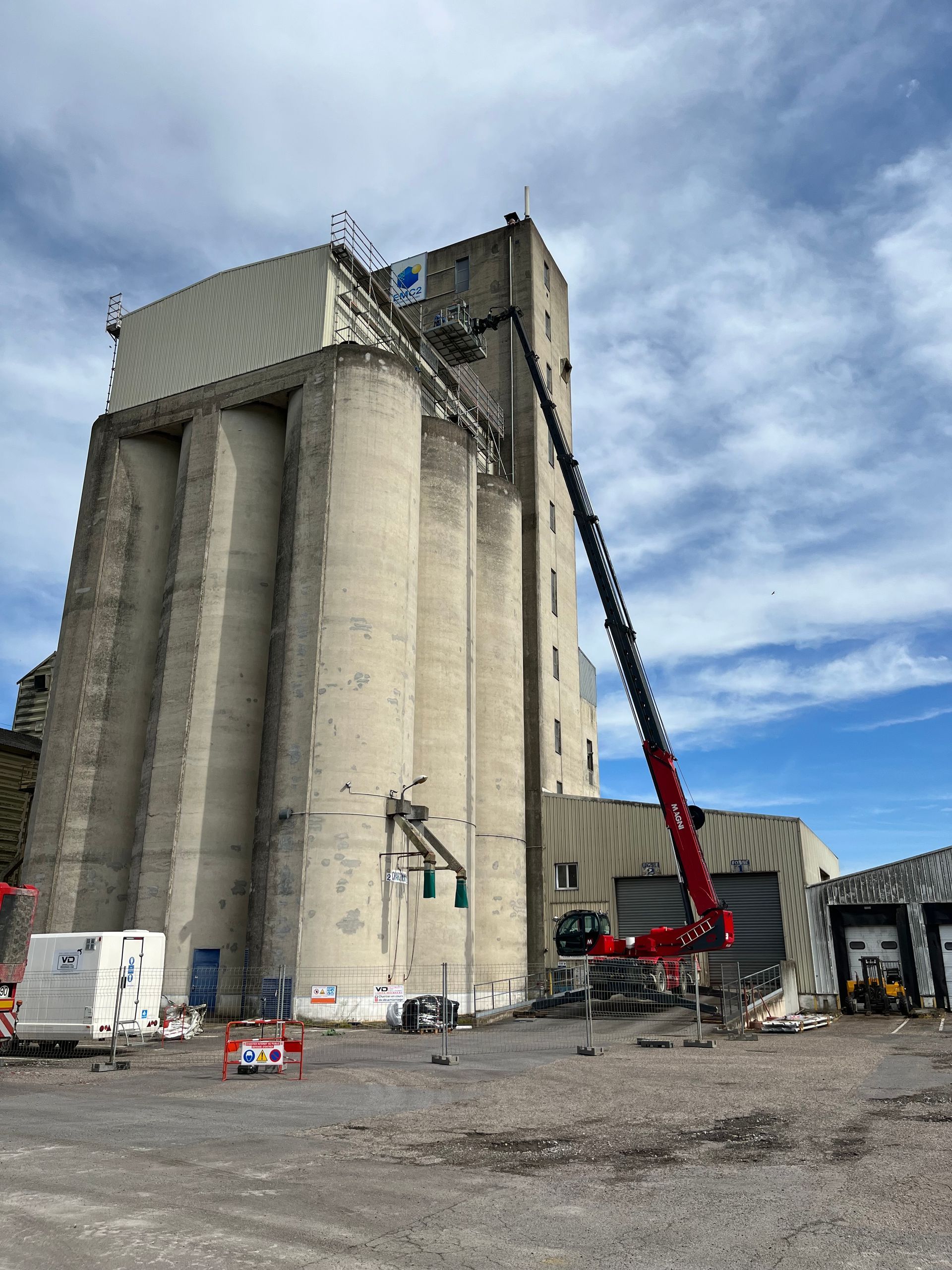 Chariot rouge Magni monté sur stabilisateur araignée avec nacelle déployée pour intervenir sur un gand silot en béton