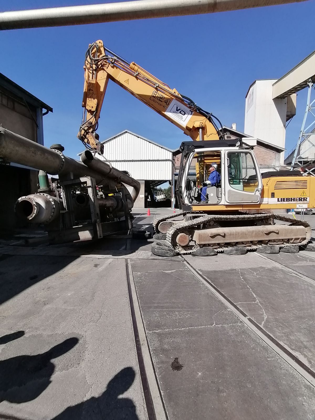 Pelleteuse jaune en train de soulever une énorme structure métallique