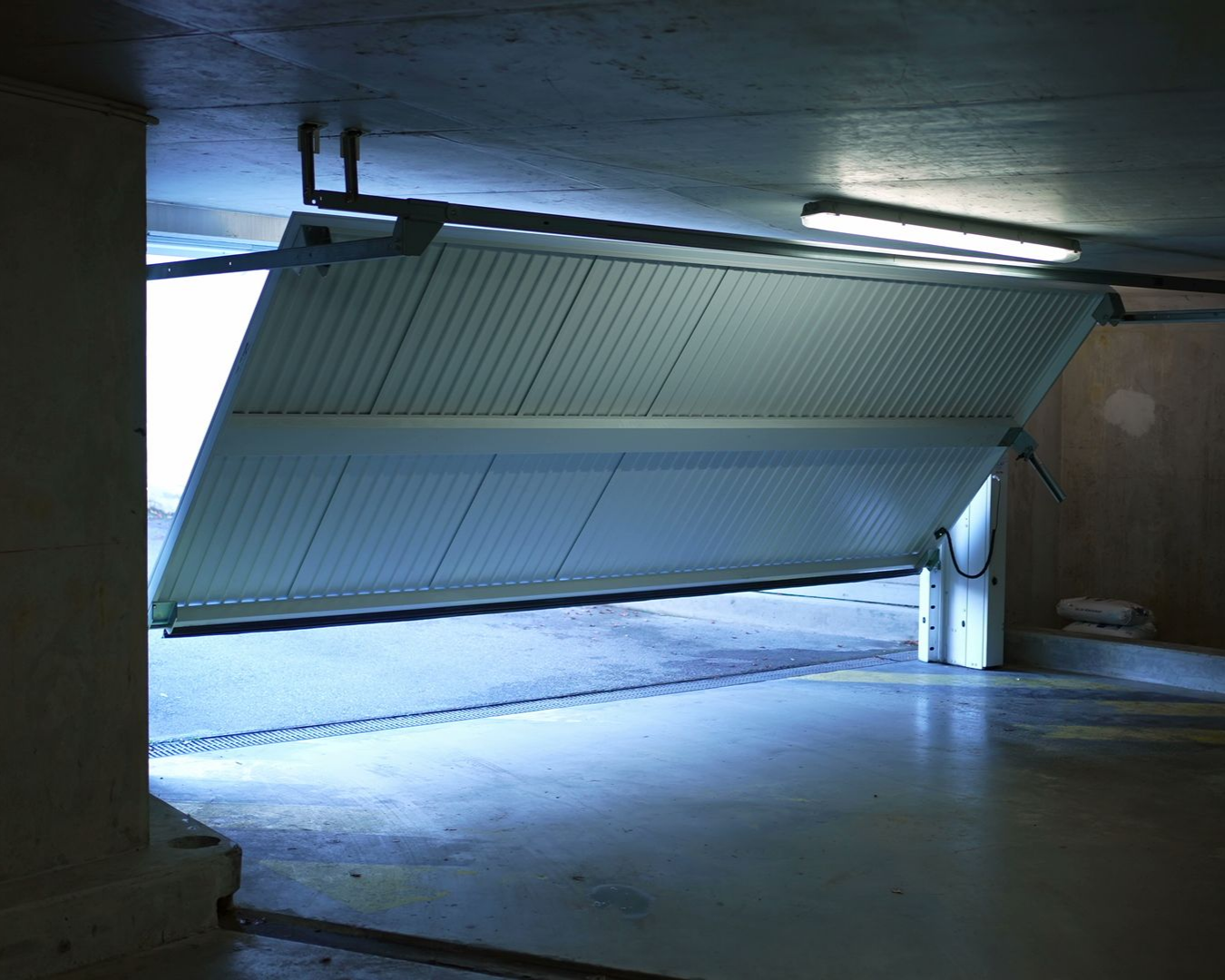 Porte de garage entrouverte laissant entrer une lumière vive dans un garage.