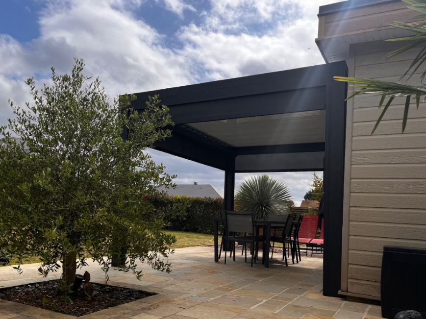 Patio couvert avec pergola noire, table à manger extérieure et façade beige.
