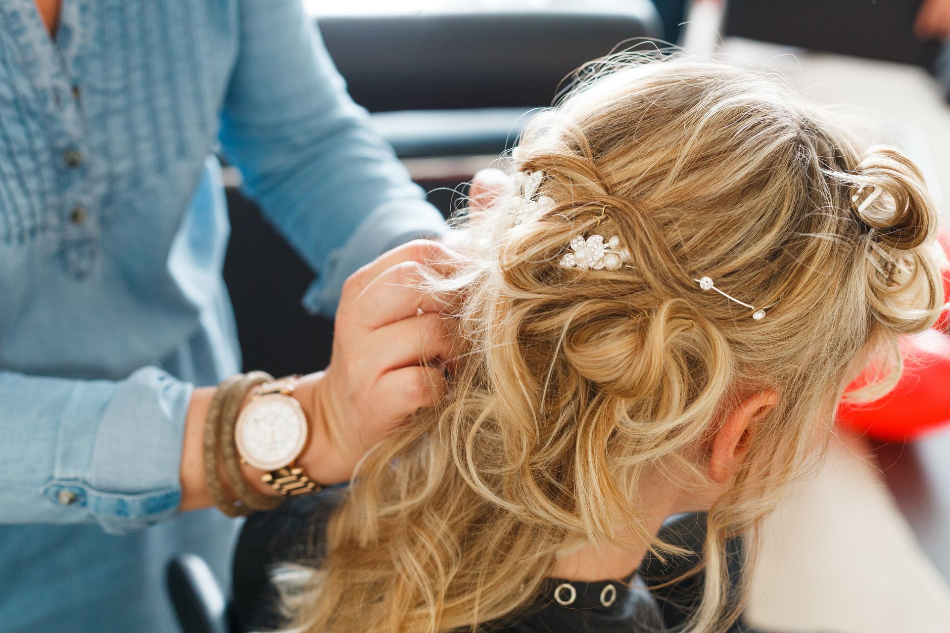 Eine Stylistin steckt einer Person dekorative Haaraccessoires in die blonde Hochsteckfrisur.