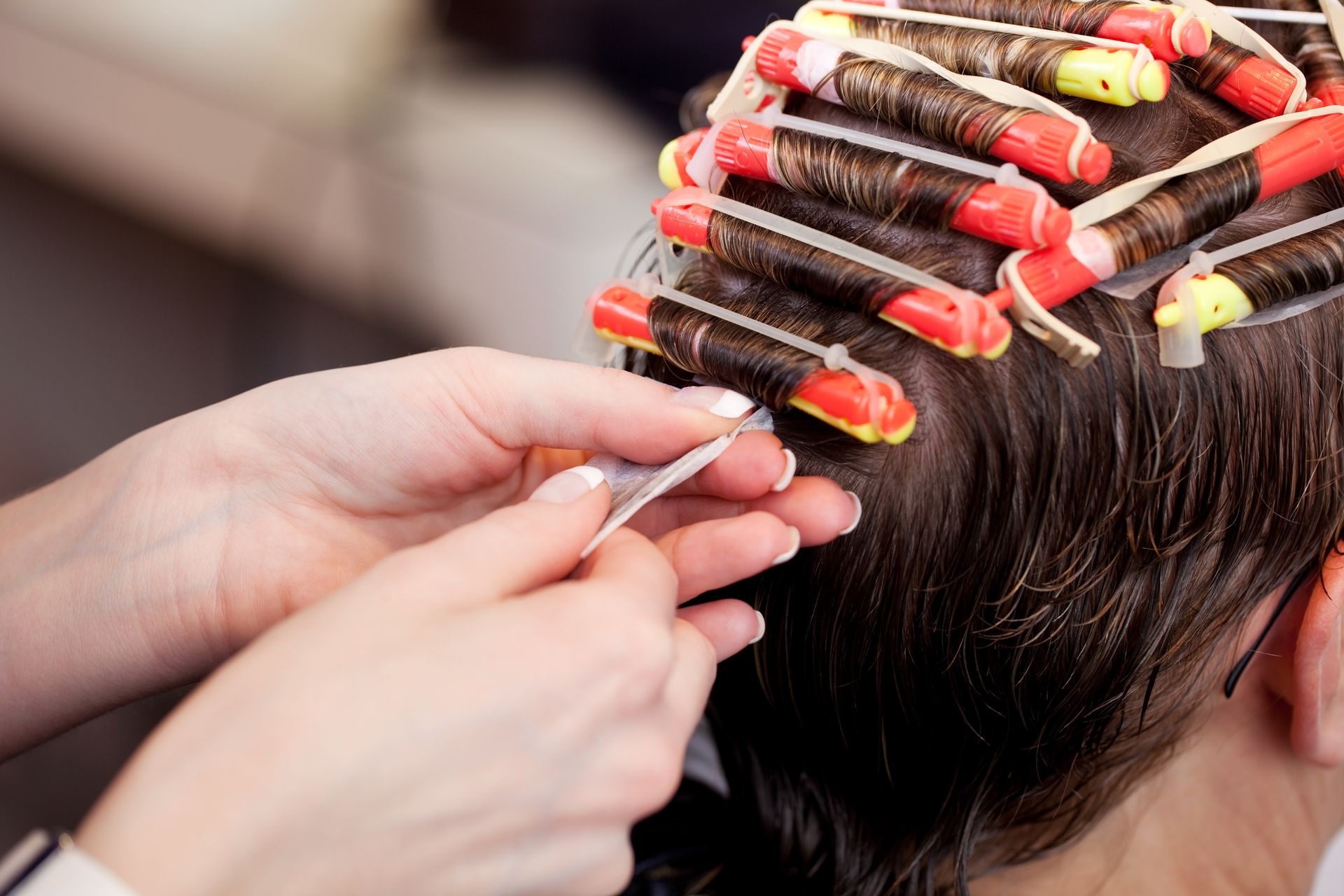 Hände wickeln Haare um Dauerwellenstäbe, Nahaufnahme des Kopfes einer Person in einem Salon.