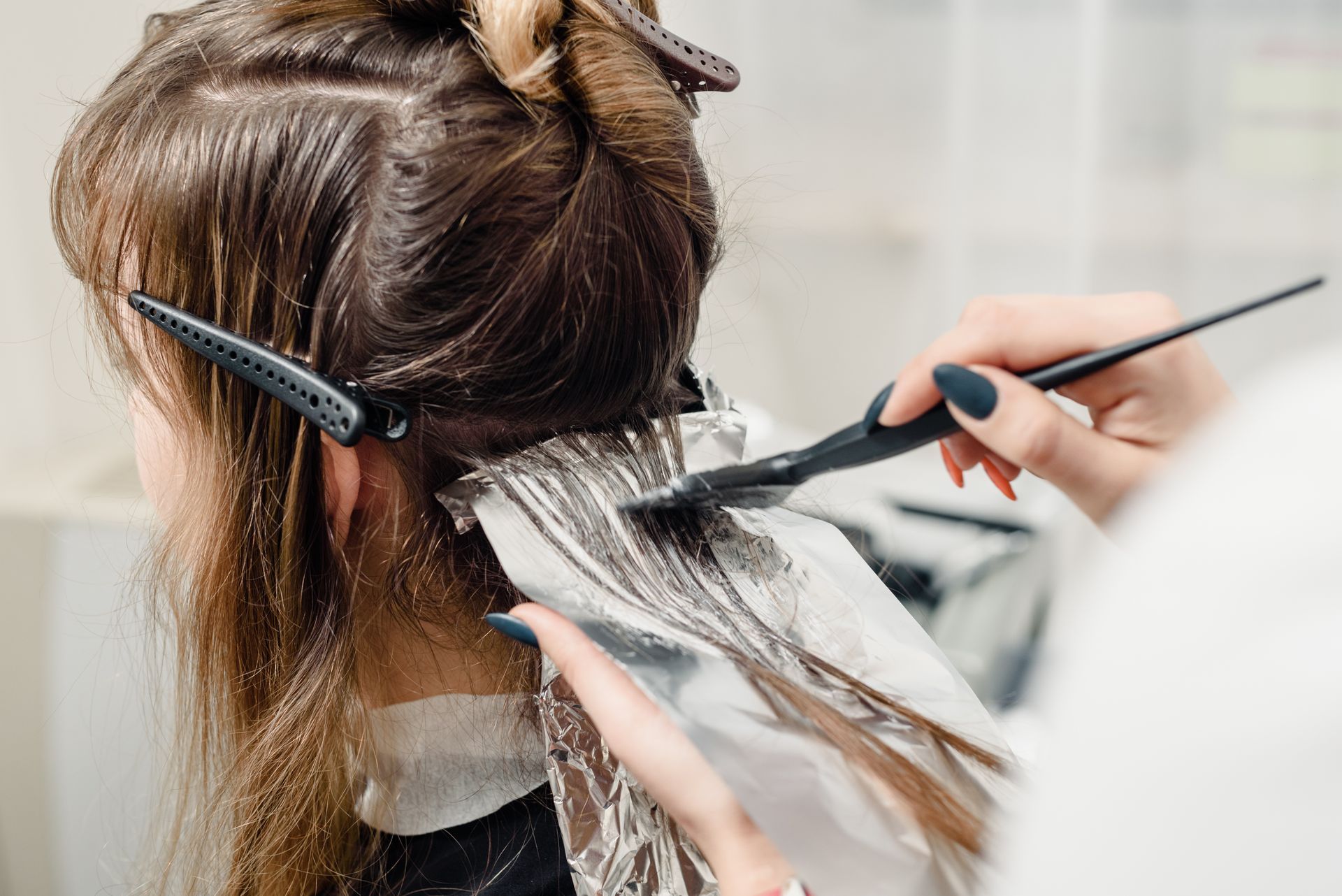 Person, die sich in einem Salon mit Folie und Bürste Strähnchen ins Haar zaubern lässt.