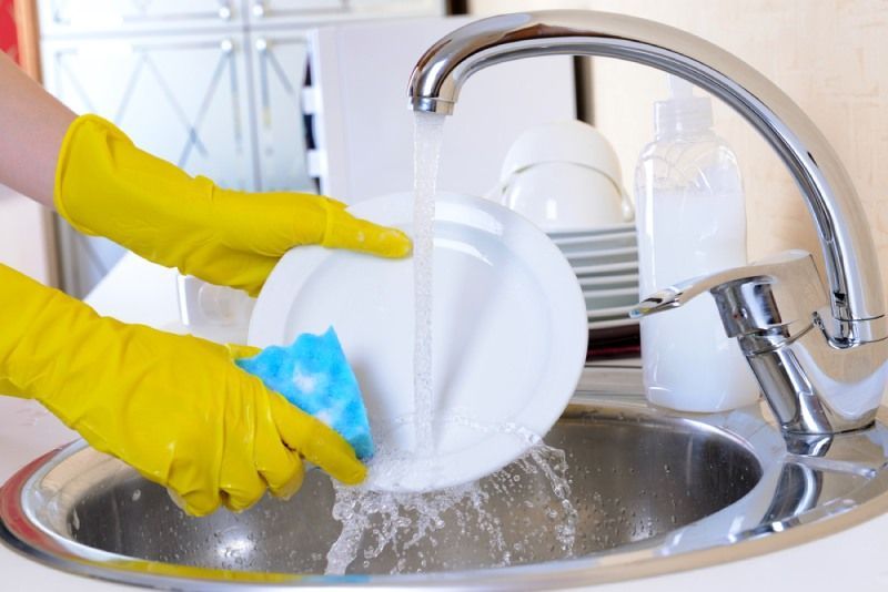 Küchenhilfe mit gelben Handschuhen spült das Geschirr ab