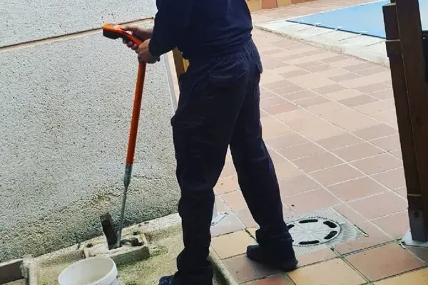 Un hombre está limpiando la acera con una manguera y un balde.