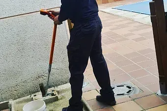 Un hombre está limpiando la acera con una manguera.