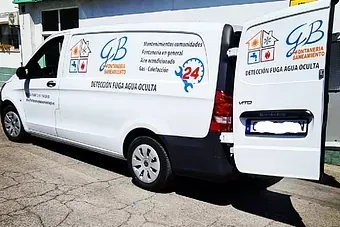 Una furgoneta blanca con las puertas abiertas está estacionada frente a un edificio.