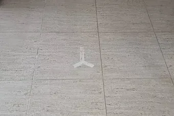 Un triángulo blanco está pintado sobre un suelo de baldosas.