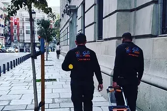 Dos hombres caminan por una acera frente a un edificio.