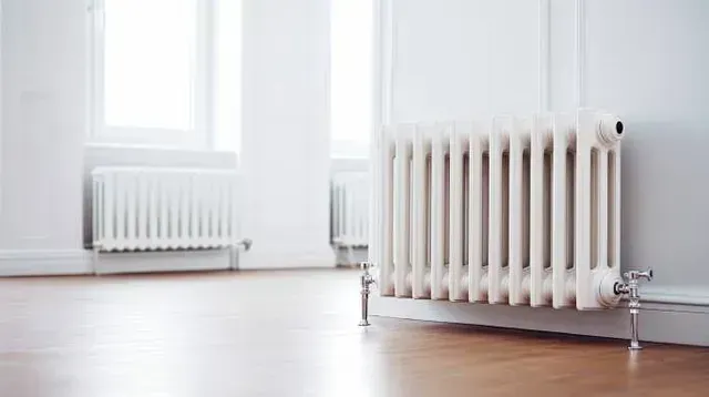 Un radiador blanco está en una habitación vacía al lado de una ventana.
