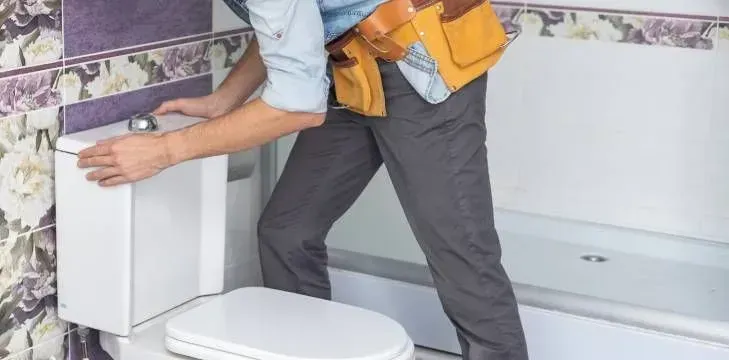 Un hombre está arreglando un inodoro en un baño.