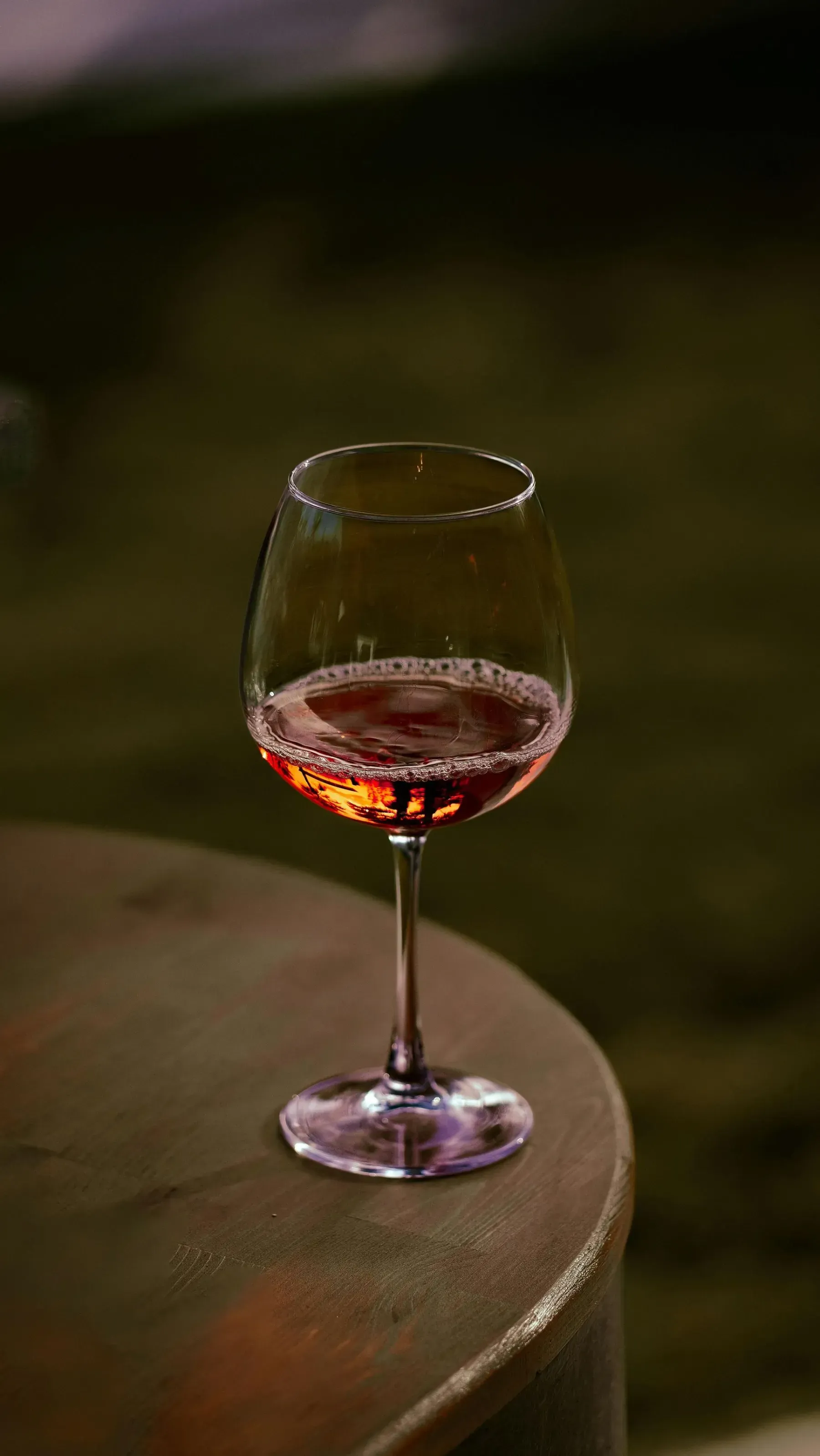 Una copa de vino rosado sobre una mesa redonda con un fondo oscuro difuminado.