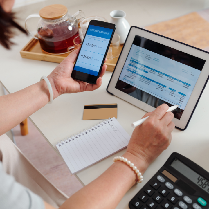 Persona revisando finanzas en teléfono y tableta con tarjeta de crédito y calculadora.