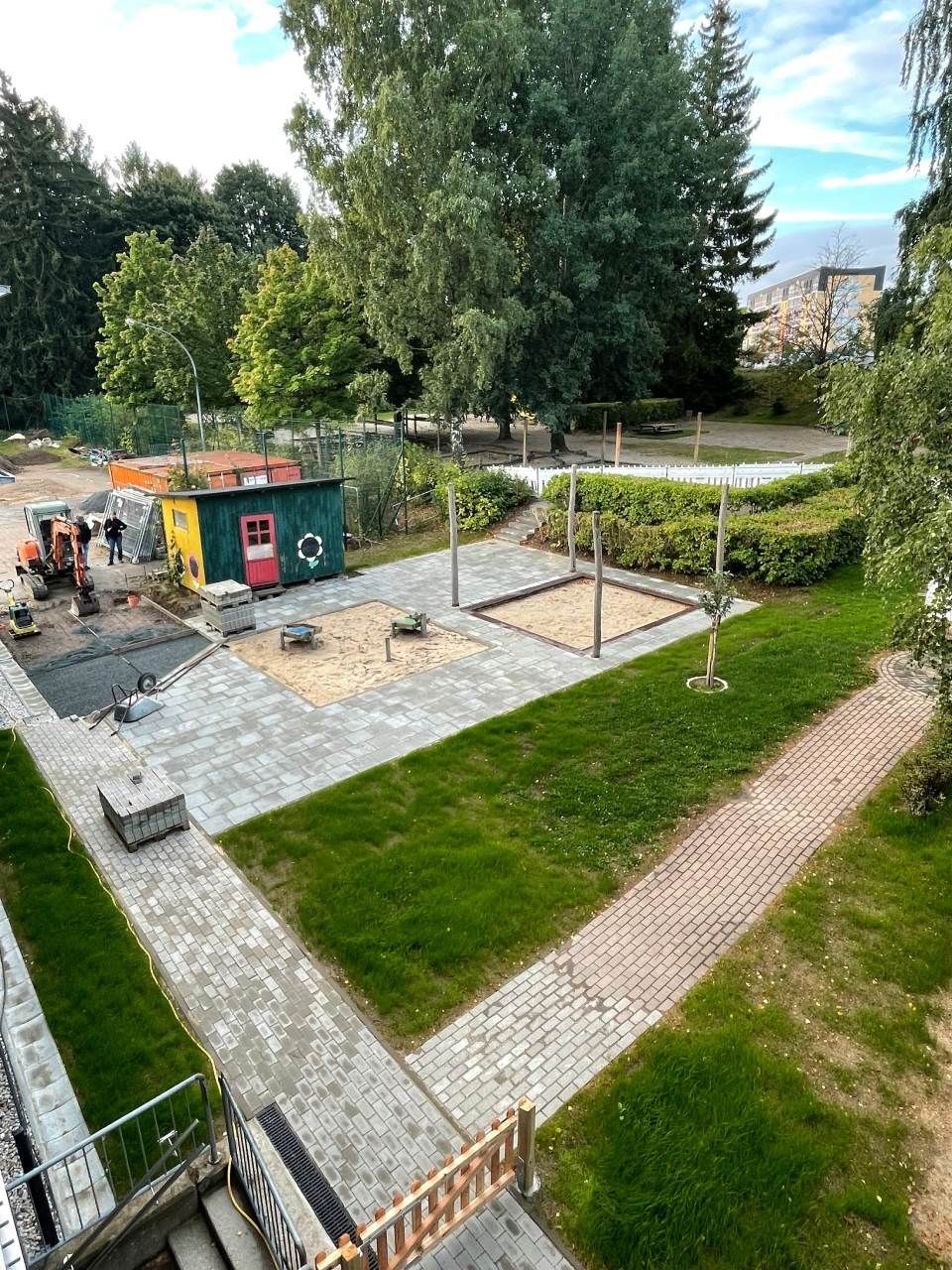 Baustelle mit neu gepflasterten Flächen, Rasen, Sandkasten und kleinem Schuppen im Freien.