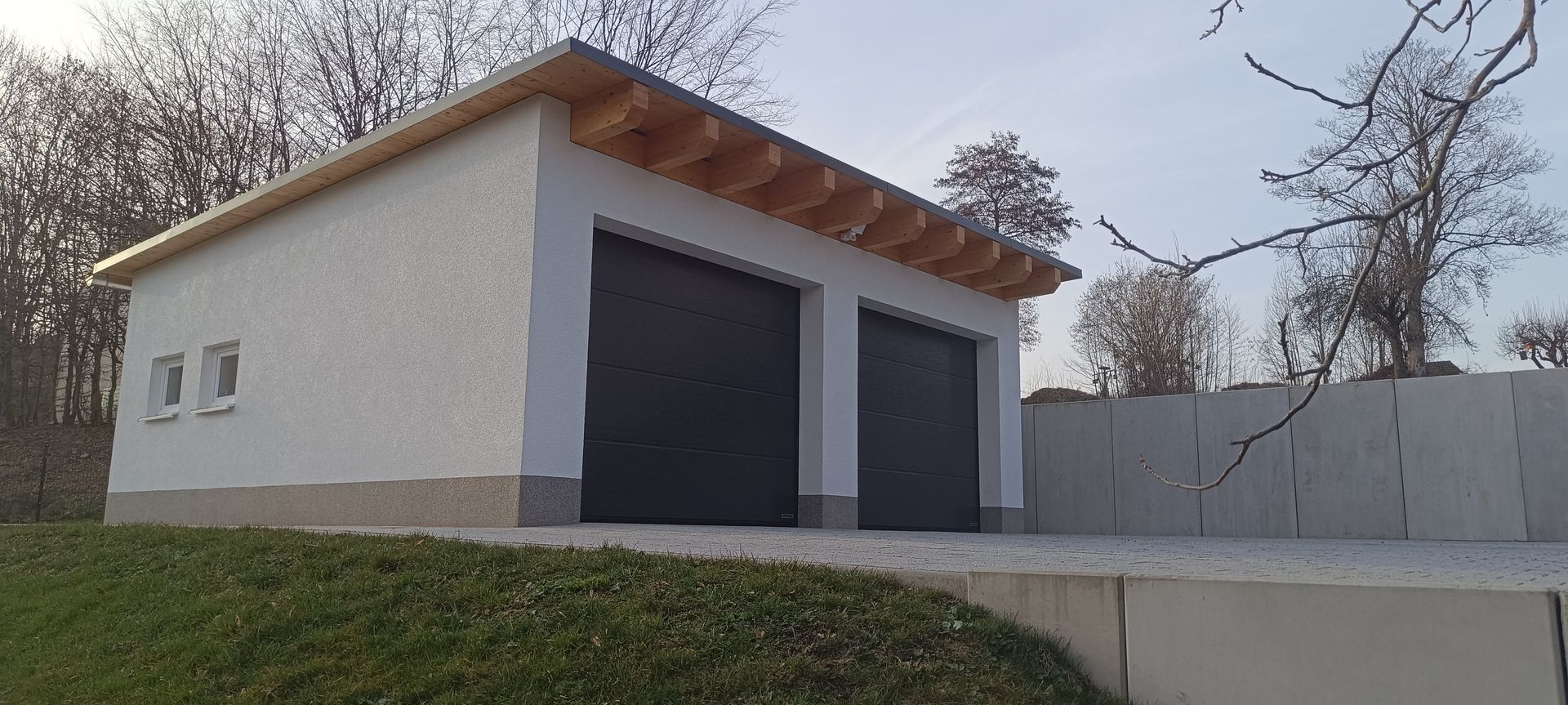 Sitzbereich im Freien mit Sonnenschirmen, Bänken und einem großen Baum neben einem hellen Gebäude.