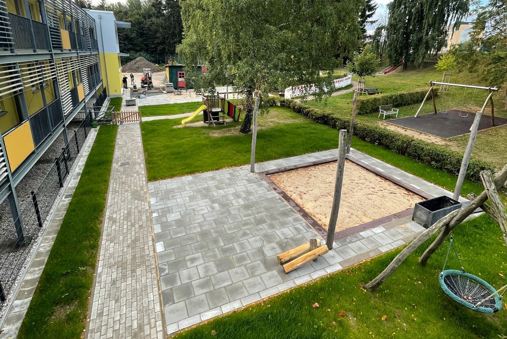 Fassade eines Gebäudes mit Steinsockel und einem zu einer braunen Tür führenden Gehweg; Fenster in den oberen Geschossen.
