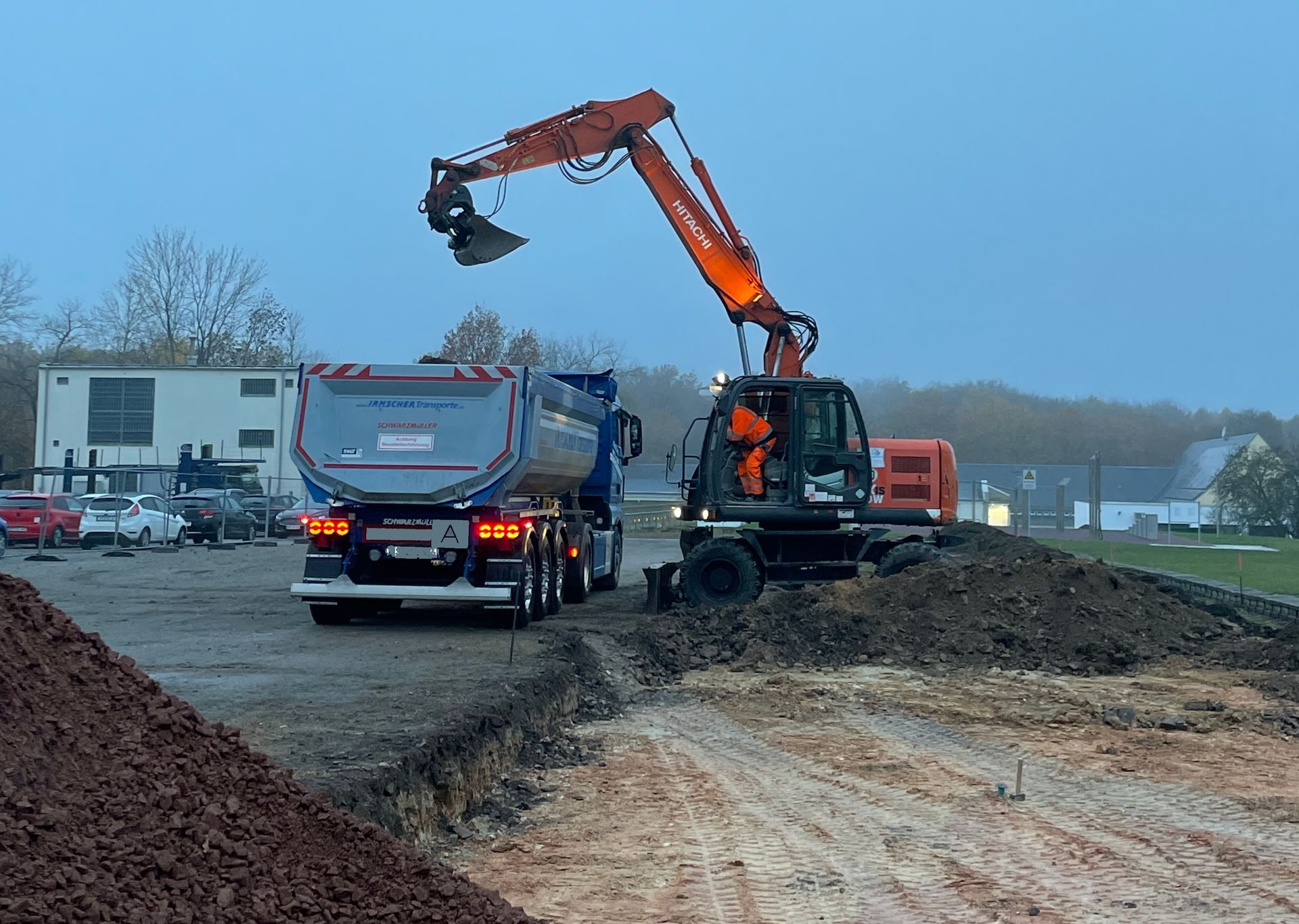 Außenbereich mit Gebäuden, Pflasterung, einer niedrigen Mauer und einem gelben Mülleimer.