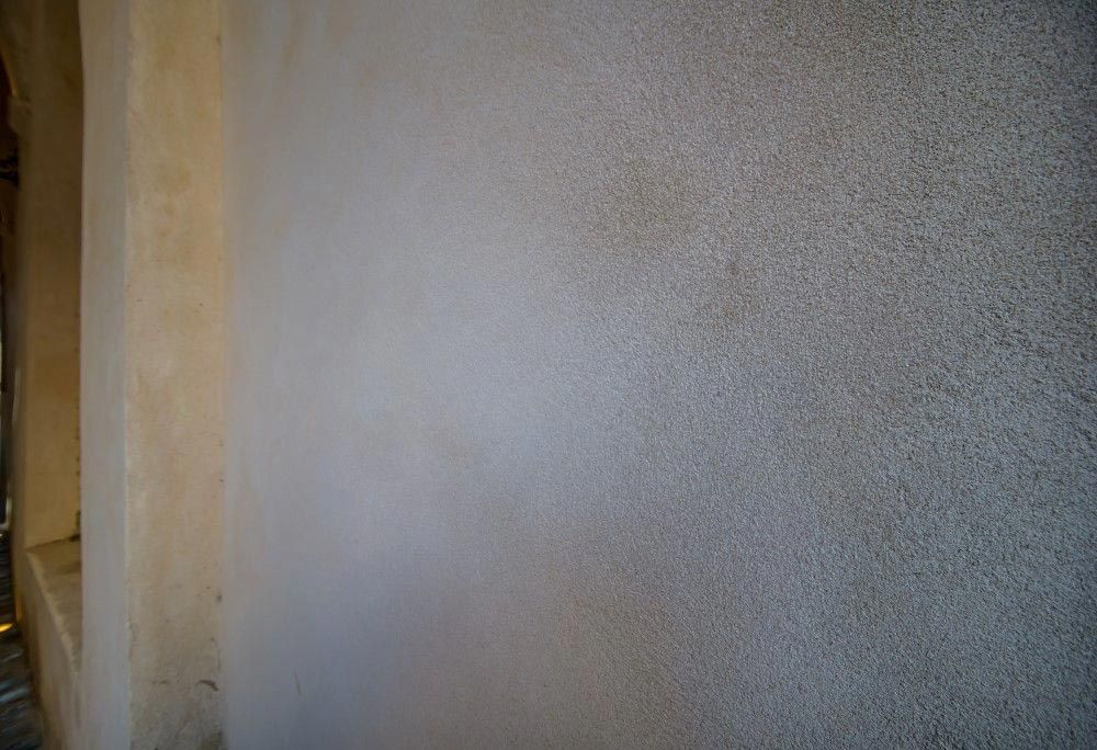 Primer plano de una pared beige texturizada junto a una puerta estrecha con luz cálida.