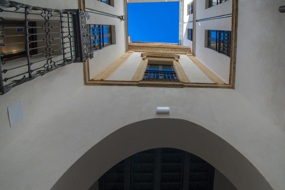 Vista del patio interior mirando hacia el cielo azul a través de balcones abiertos y arcos blancos.