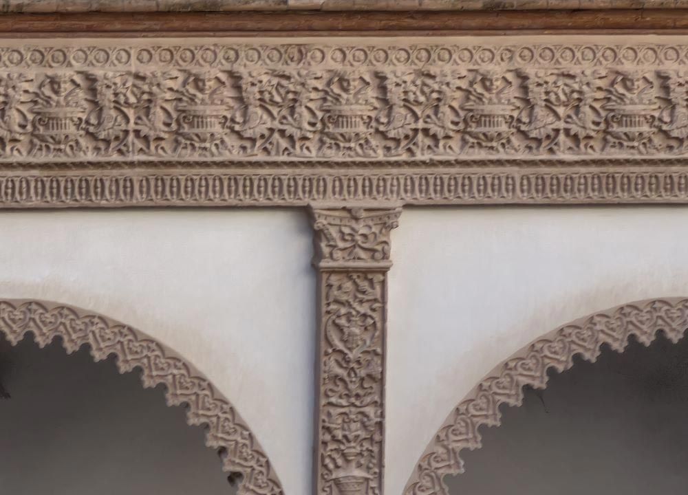 Arco de piedra tallada ornamentada con friso decorativo y arcos festoneados en un interior histórico.