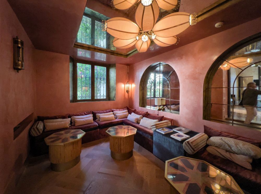 Acogedor salón de terracota con sofá curvo, taburetes, ventanas arqueadas y un gran ventilador de techo.