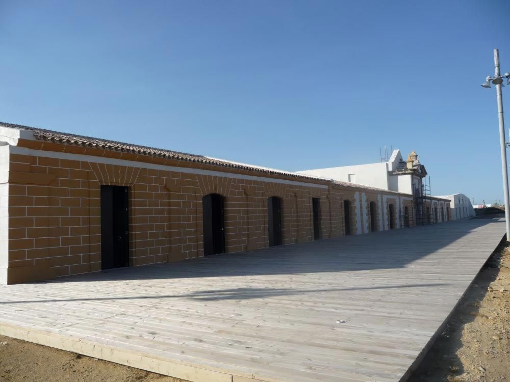 Un largo paseo marítimo de madera junto a un edificio de ladrillos bajo un cielo azul despejado.