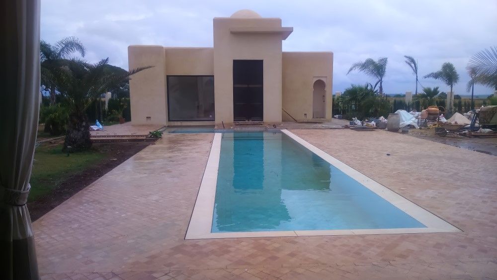 Casa moderna de color beige con una larga piscina de azulejos azules en un patio pavimentado.