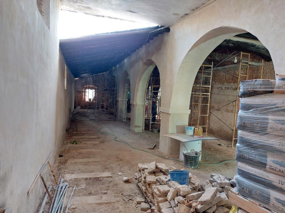 Pasillo parcialmente construido con arcos blancos, suelo de tierra y materiales de construcción apilados a lo largo del lado derecho.