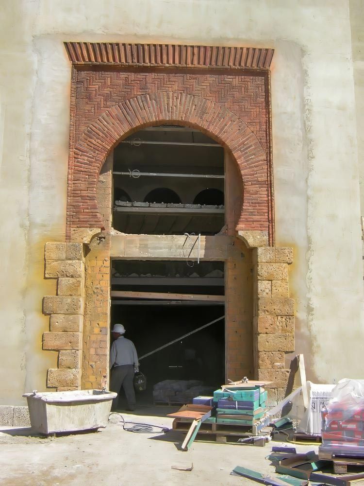 Antigua entrada con arco de ladrillo en la fachada de un edificio, con materiales de construcción apilados en el exterior y un trabajador en el interior.