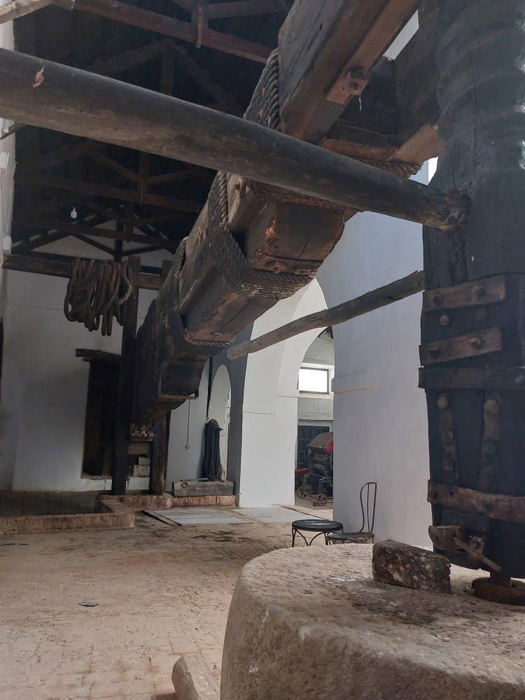 Interior de un antiguo molino industrial con vigas de madera, maquinaria de gran tamaño y suelo de piedra desgastada.