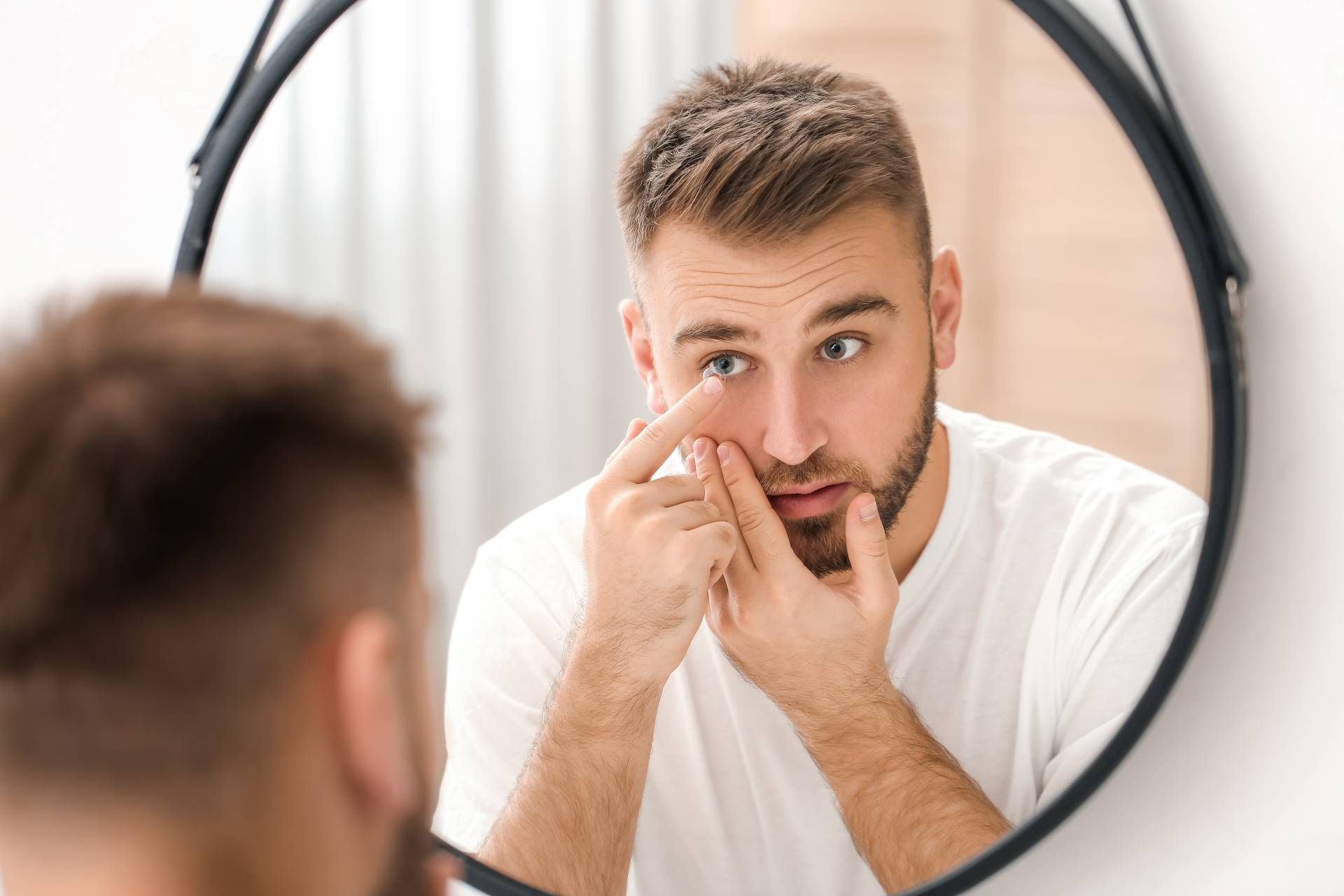 Ein Mann trägt eine Kontaktlinse und schaut in den Spiegel