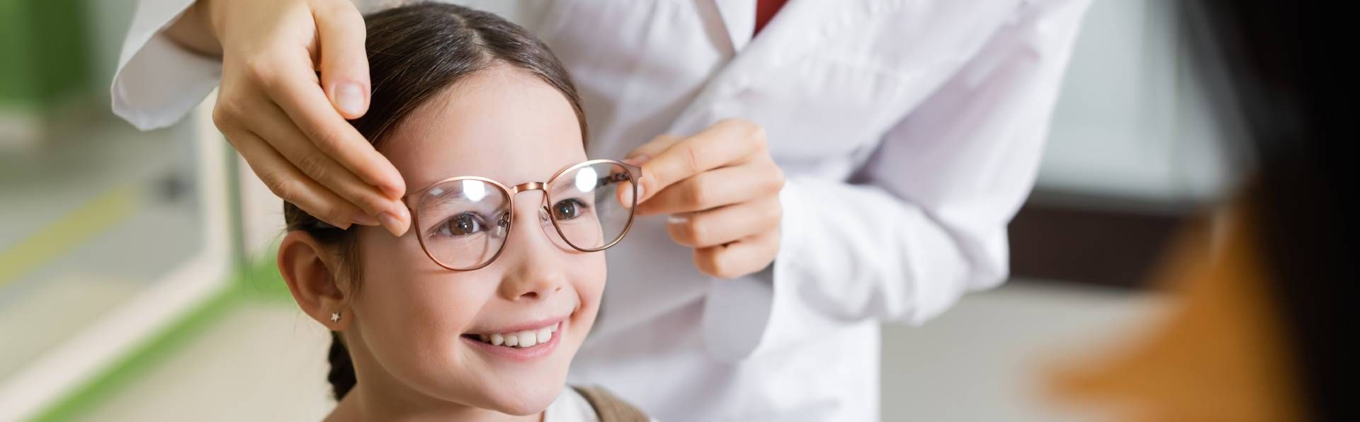 Ein kleines Mädchen lächelt , während ein Arzt ihr eine Brille anzieht