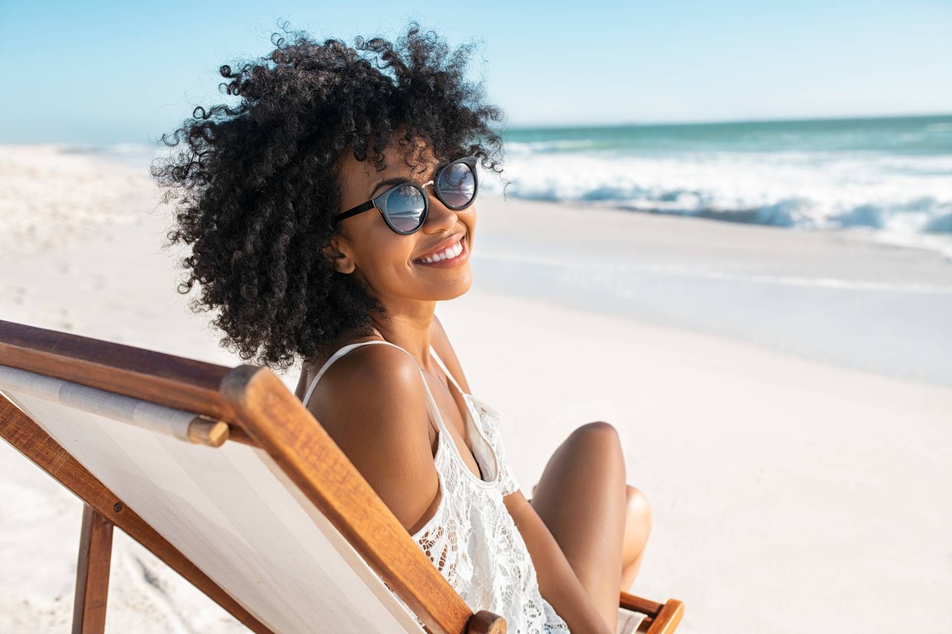 Eine Frau sitzt in einem Liegestuhl am Strand und lächelt