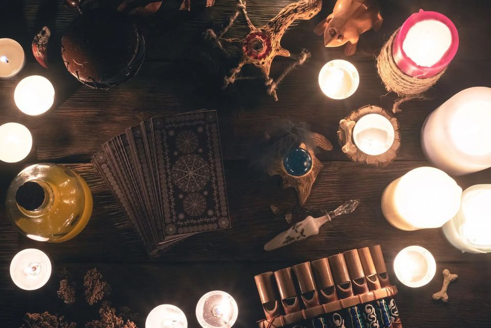 Las velas rodean cartas de tarot, cristales y frascos de pociones en una mesa de madera, lo que sugiere un entorno espiritual.