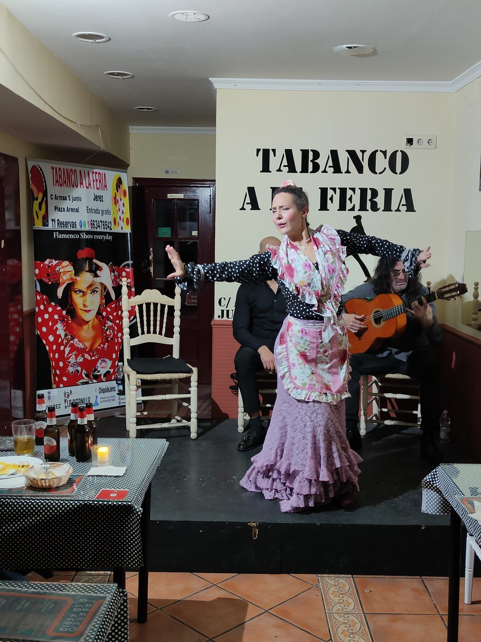 Una mujer con un traje de flamenca baila en un escenario frente a un cartel que dice "tabanco a feria"