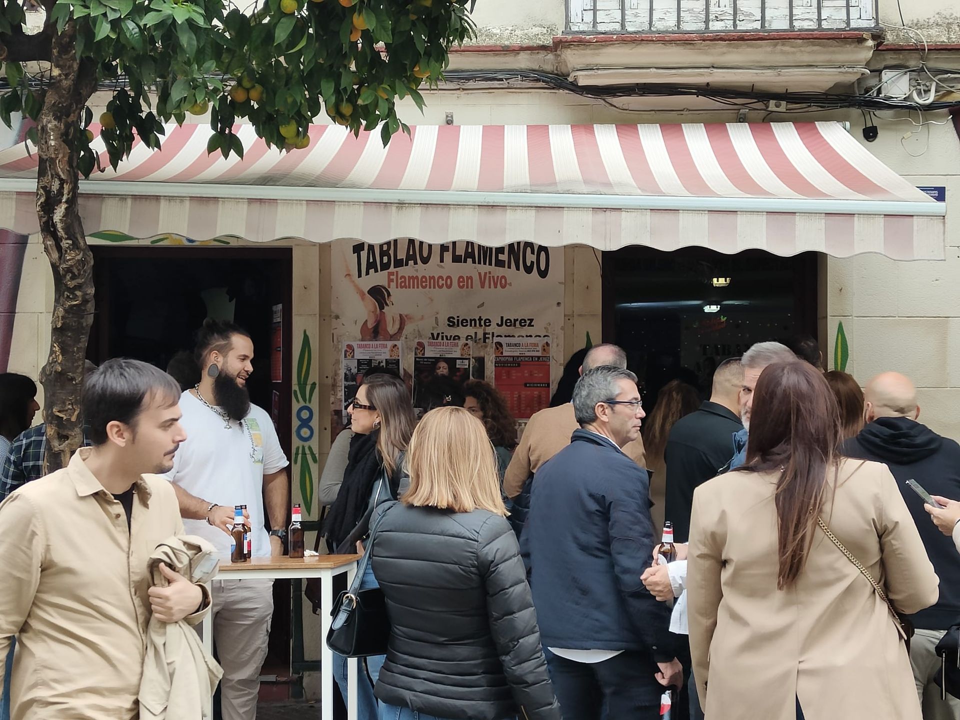 Un grupo de personas se encuentra afuera de un restaurante con un toldo a rayas.