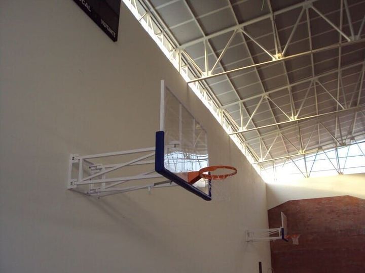 Um ginásio poliesportivo coberto com piso verde, painéis de madeira nas paredes e duas cestas de basquete.