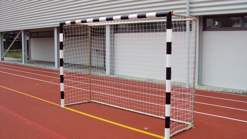Uma baliza de andebol com postes listrados em preto e branco está localizada numa pista de atletismo vermelha 