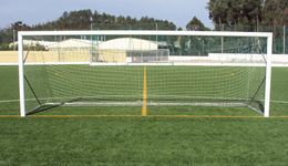 Um gol de futebol branco com rede posicionado em um campo de grama verde com linhas pintadas de amarelo.