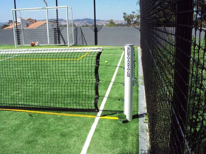 Uma baliza de handebol listrada em preto e branco, com uma rede, está posicionada no chão de um ginásio 